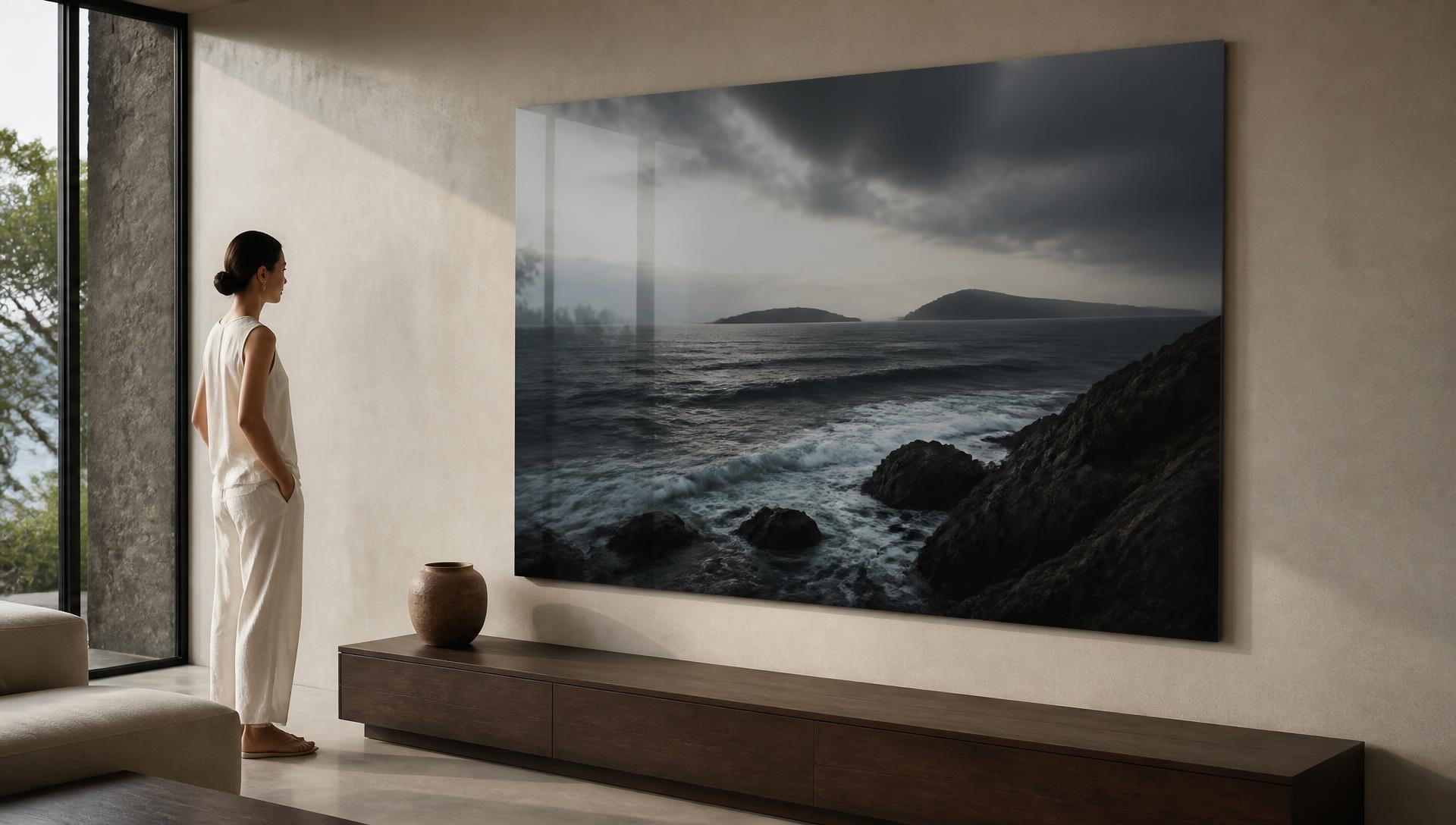 A large glossy metal print of a coastal seascape on a pale wall in a contemporary interior, with daylight raking across its surface